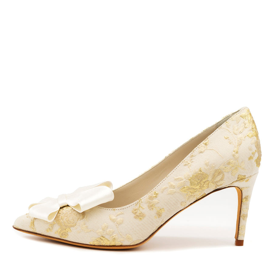 A pointed toe satin pump with a bow detail on the toe box and a stiletto heel, primarily in a white or light color with gold accents.