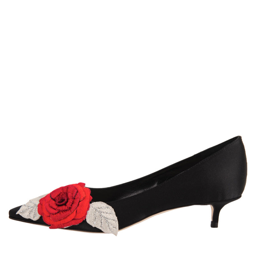 A black satin pointed-toe heel with a red floral decoration on the top and a small kitten heel.
