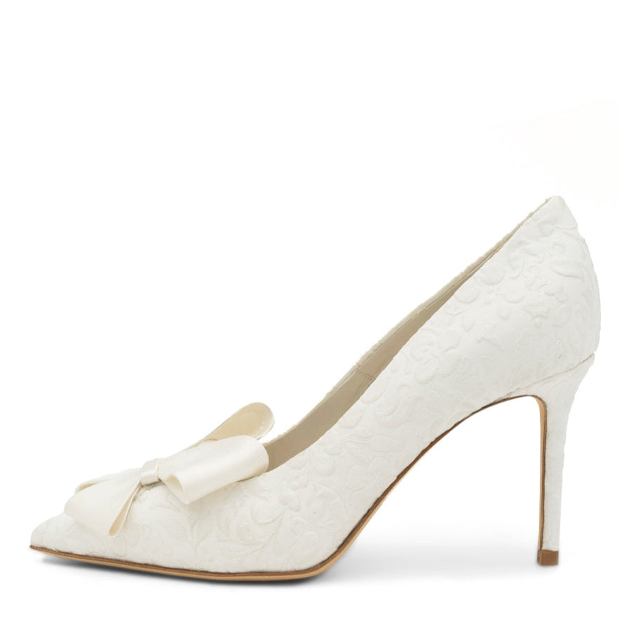 A white, pointed toe pump with a fabric upper and leather insole and lining, displayed against a plain background.