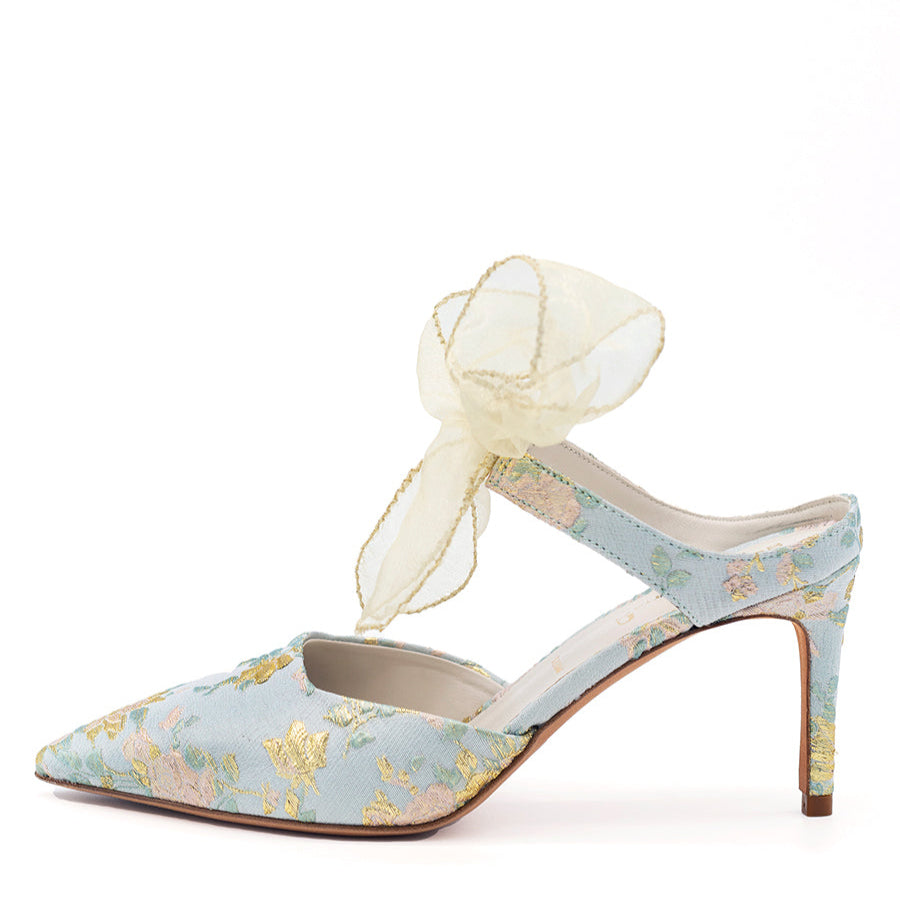 A blue floral fabric pointed toe pump with a slip on mule silhouette and a sheer bow detail.